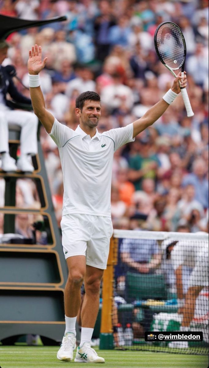 a male tennis player is holding his racket in the air and waving to the crowd