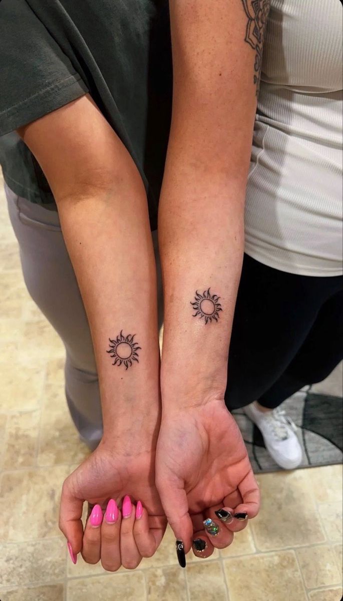 two people holding hands with tattoos on their arms and one has a sun tattoo on the wrist