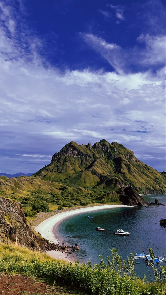 boats are on the water in front of an island with green hills and blue sky