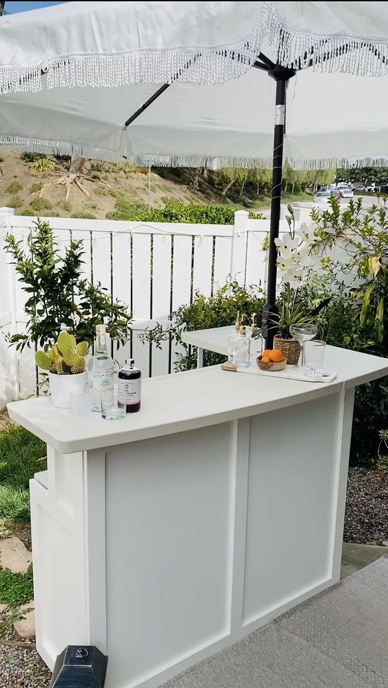 an outdoor bar is set up with drinks and bottles on it, under an umbrella