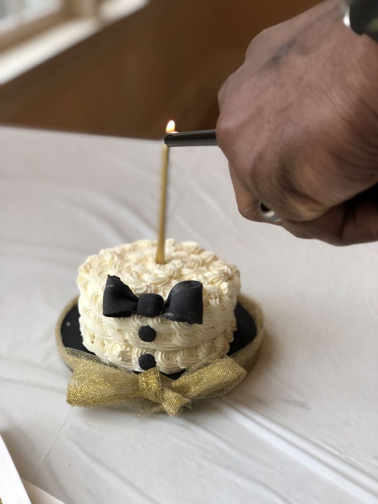 a person lighting a candle on top of a cake with a bowtie and bow tie