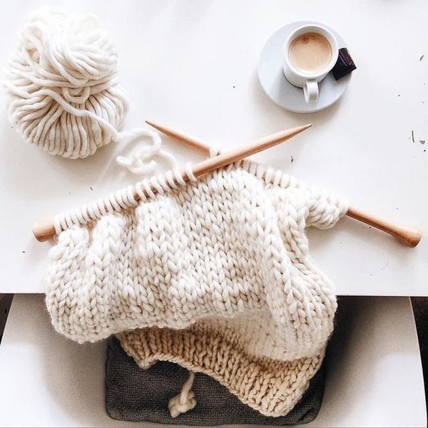 two knitting needles are next to a white sweater and cup of coffee on a table