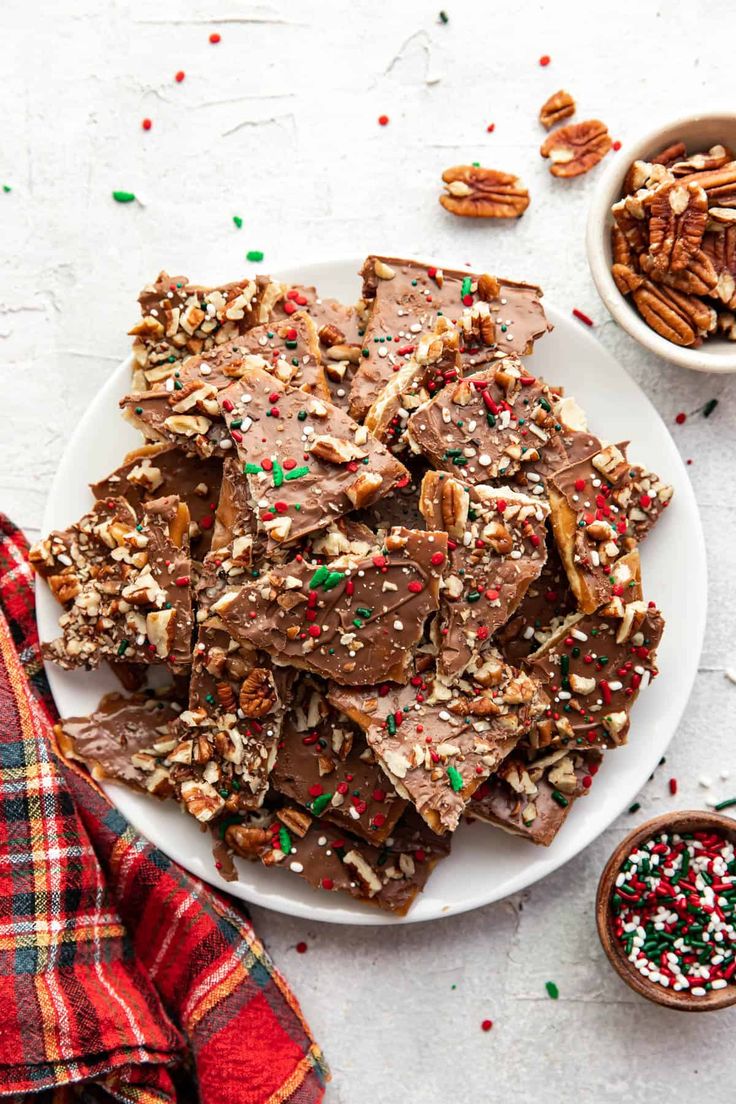 a white plate topped with pieces of chocolate fudge next to bowls of pecans