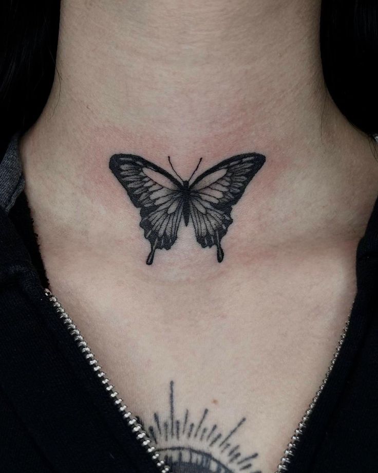 a woman's chest with a butterfly tattoo on her upper arm and lower neck