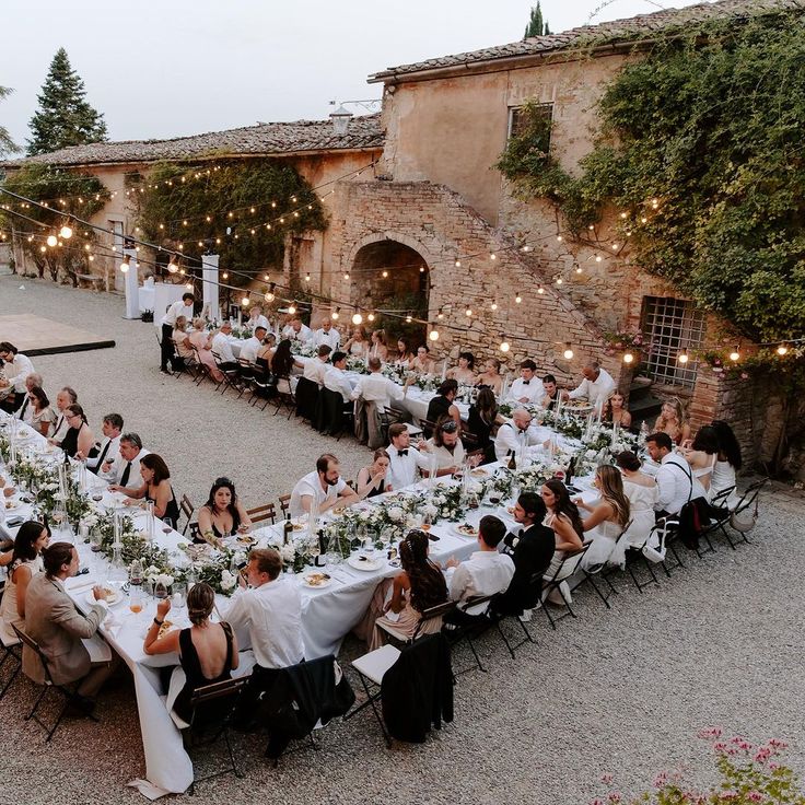 a large group of people sitting at tables in front of an old building with lights