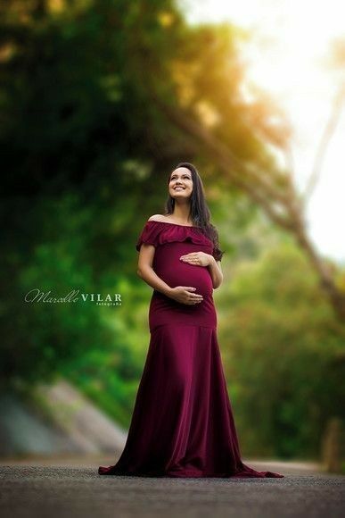 a pregnant woman standing in the middle of a road wearing a maroon dress and smiling