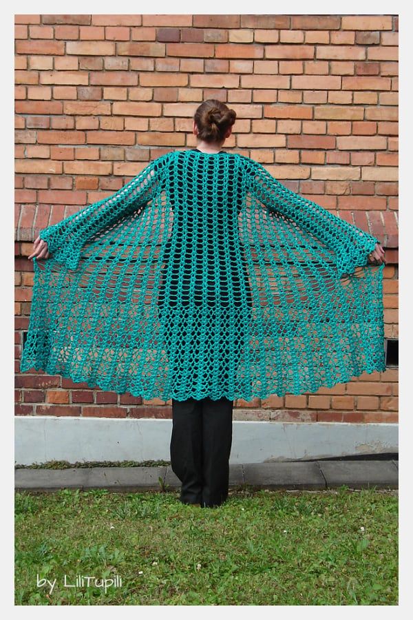 a woman standing in front of a brick wall wearing a green crocheted shawl