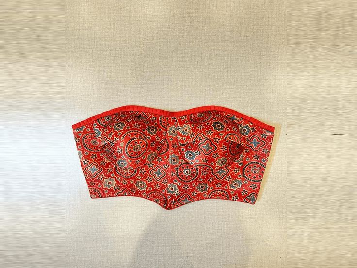 Shop stunning red Ajrak corset blouse online in USA. Elevate your saree style with exquisite readymade saree blouses, embroidered saree blouses, Banarasi saree blouse, designer saree blouse, choli-cut blouses, corset blouses from Pure Elegance Indian clothing store in USA.-full view Fitted Red Kalamkari Print Blouse Piece, Red Fitted Choli With Kalamkari Print, Fitted Red Choli With Kalamkari Print, Fitted Red Tops With Kalamkari Print, Fitted Red Kalamkari Print Tops, Festive Red Kalamkari Print Top, Festive Red Kalamkari Tops, Fitted Red Choli For Festivals, Fitted Bohemian Bandhani Print Top