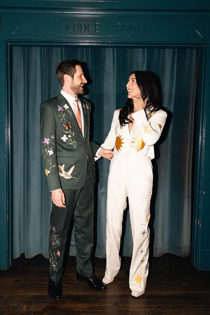 a man and woman standing next to each other in front of a blue curtain holding hands