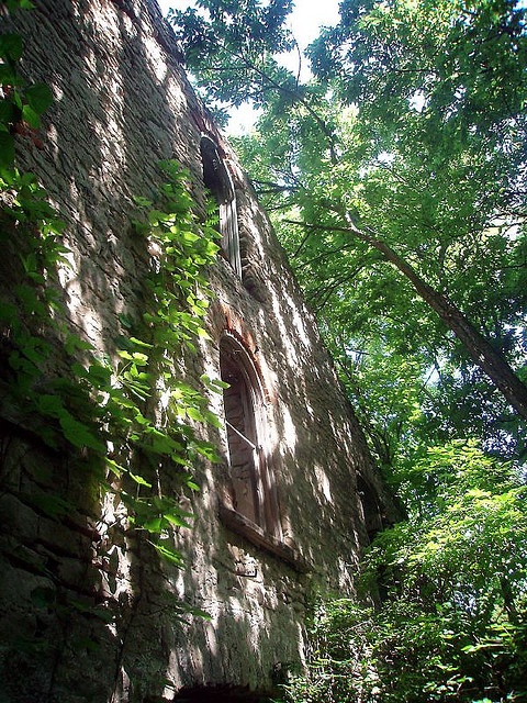 an old brick building surrounded by trees in the sun with lots of leaves on it