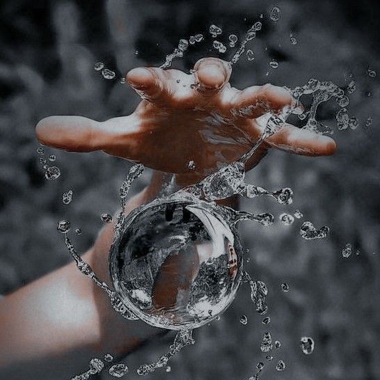 a person's hand holding an object in the air with water splashing on it