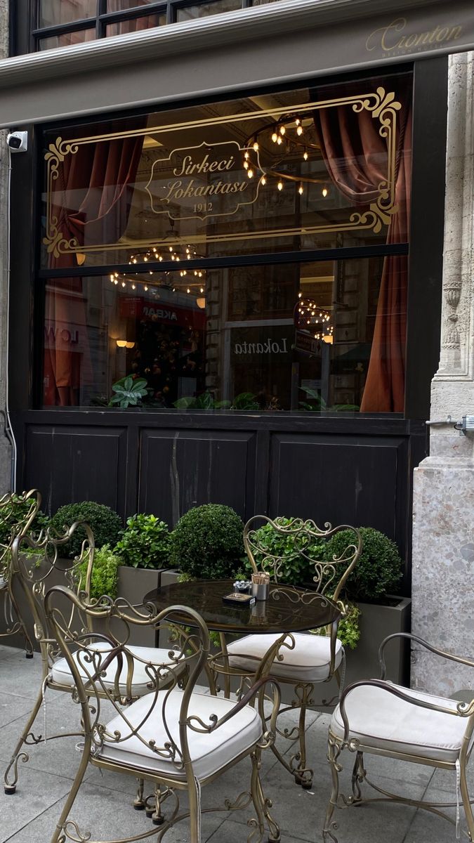 tables and chairs in front of a restaurant with lights strung from the building's windows