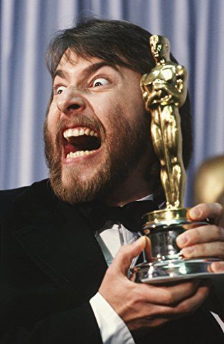 a man in a tuxedo is holding an oscar statue and yelling with his mouth wide open