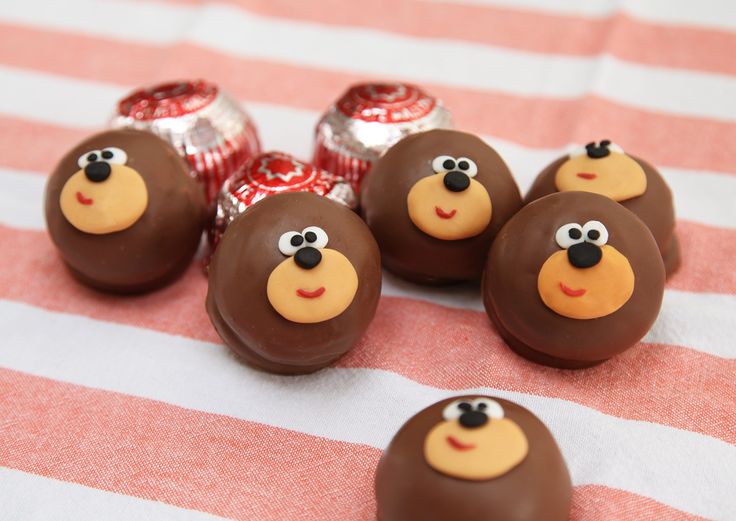 chocolate candies with faces on them sitting on a striped tablecloth next to candy bars