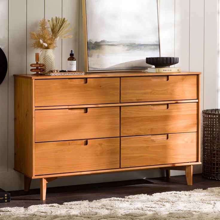 a wooden dresser sitting in front of a window next to a painting on the wall