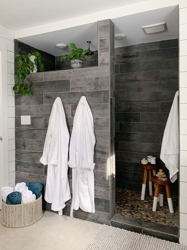 two white towels are hanging on the wall next to a gray tiled shower stall and stool