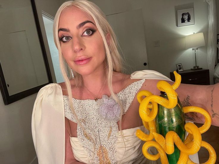 a woman in a white dress holding a vase filled with yellow plastic snake balloons and looking at the camera