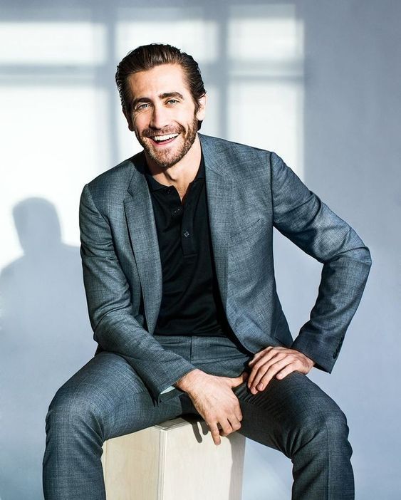 a man sitting on top of a wooden block wearing a suit and smiling at the camera