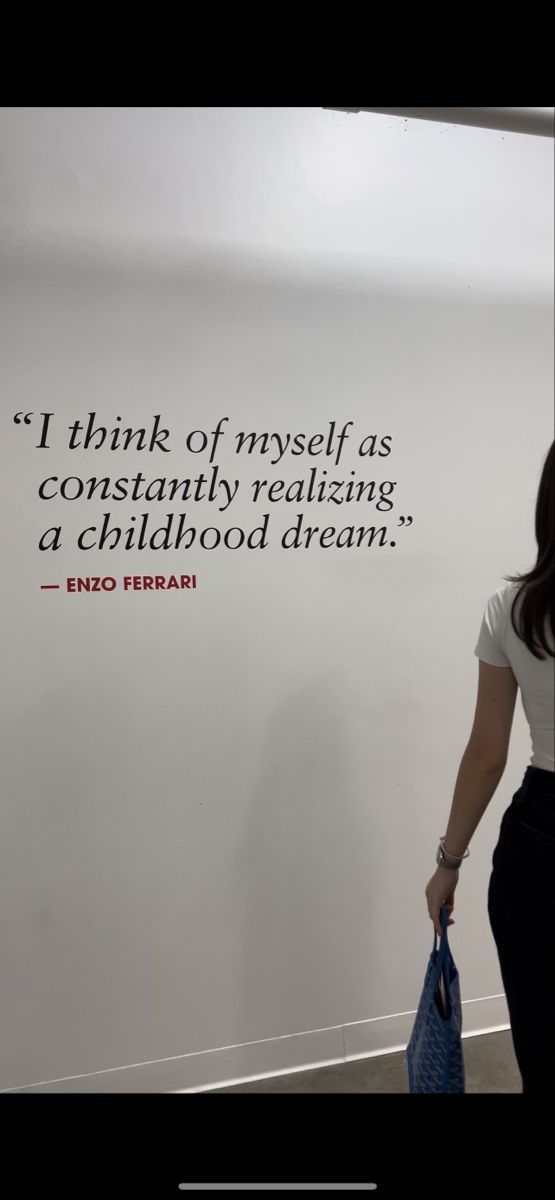 a woman walking past a white wall with a quote on the wall above her head