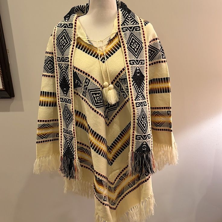 Made In Ecuador- This Beautiful Poncho Is Nwot - No Size Label - Medium 100% Wool Tassel Tie At Neck And 4” Wide Attached Scarf Tassel Trim Hem All Around Cream Background With Black Yellow Brown Orange Pattern Woven Throughout Fun Addition To Your Wardrobe - Keeps You Warm And Finishes Off Your Outfit! Length 38.5” To Longest Point Including Tassels Bin 2 Traditional Beige Poncho For Winter, Traditional White Poncho For Fall, Cream Bohemian Poncho For Fall, Beige Long Sleeve Bohemian Cape, Cream Bohemian Shawl For Fall, Traditional Long Sleeve Poncho, One Size, Traditional Long Sleeve Poncho One Size, Traditional One-size Long Sleeve Cape, Traditional Long Sleeve Cape One Size