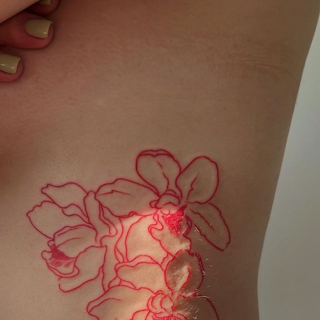 a woman's stomach with red ink on it and flowers drawn on the side