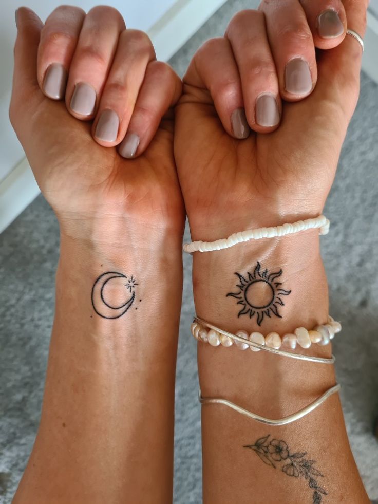 two women with matching tattoos on their arms holding hands up to each other, both wearing bracelets