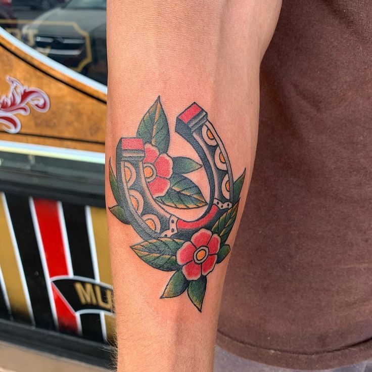 a tattoo on the arm of a man with red flowers and green leaves around it