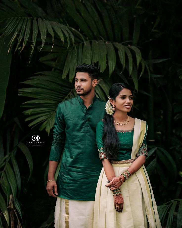 a man and woman standing next to each other in front of some palm tree leaves