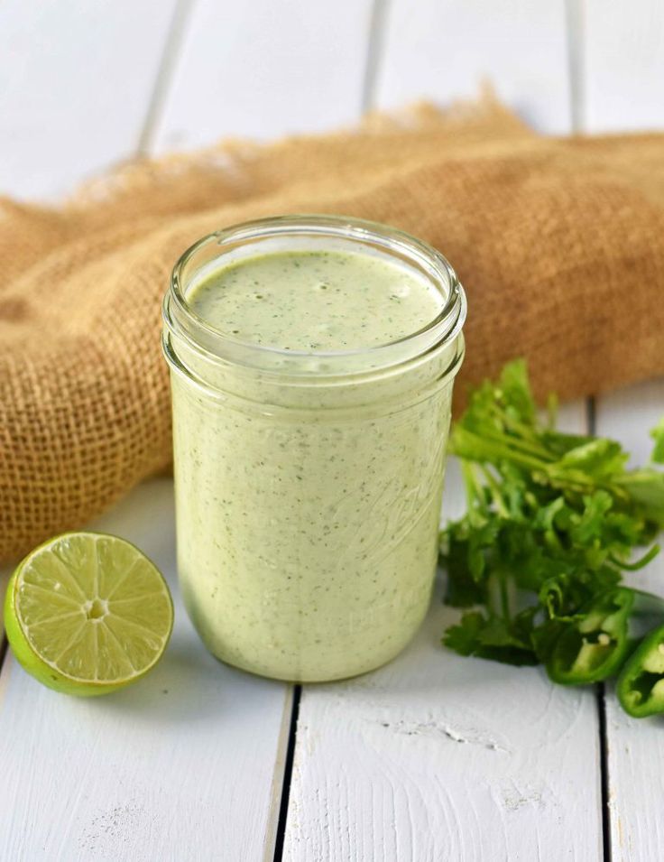 a green smoothie in a mason jar with a lime slice next to it on a white wooden table