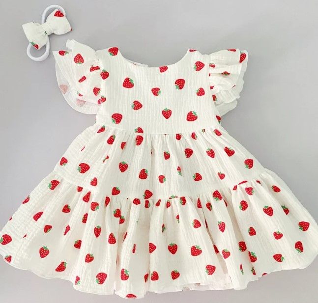 a white dress with red strawberries on it and a hair clip in the shape of a bow