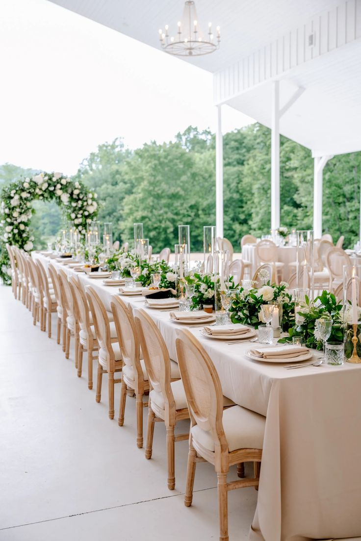 a long table is set up with white linens and greenery for an outdoor wedding reception