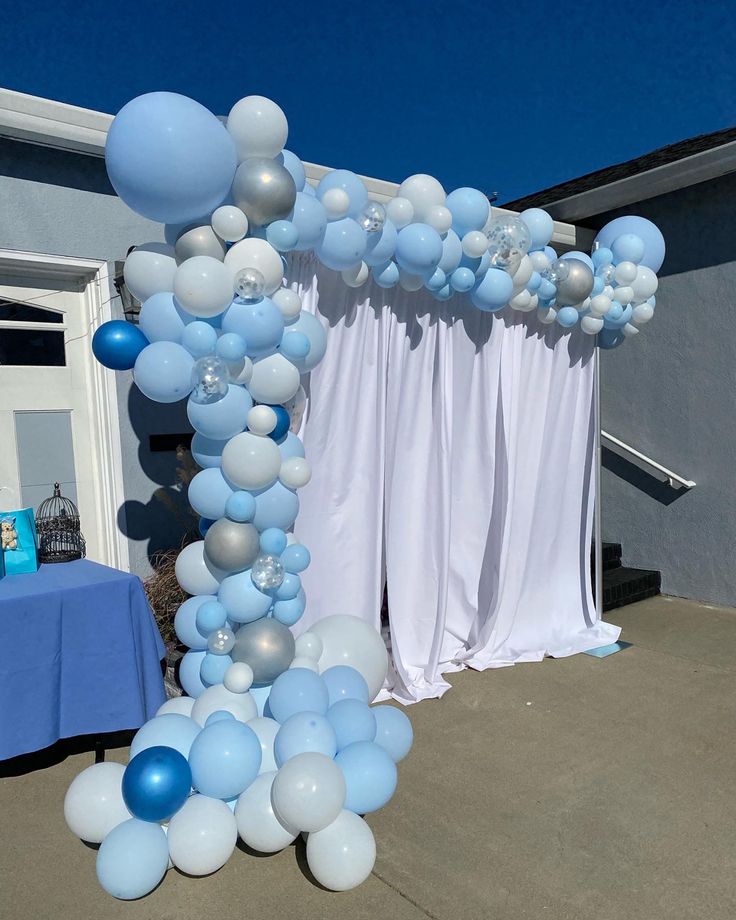 blue and white balloons are hanging from the ceiling in front of a party arch with drapes