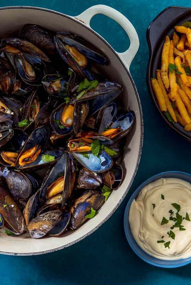 a pot full of mussels and fries next to a bowl with dip on the side