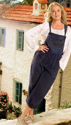 a woman standing on top of a stone wall next to a white building with green shutters