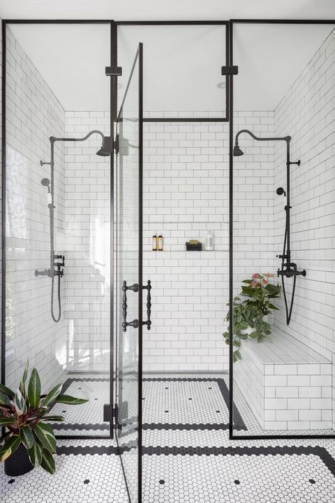 a white bathroom with black and white tile flooring, two shower stalls and a plant in the corner