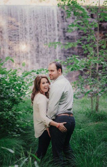 an engaged couple standing in front of a waterfall