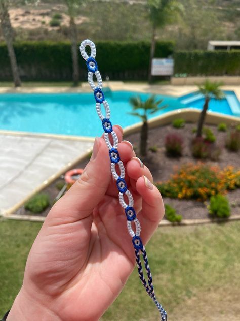 a hand holding a blue and white beaded lanyard next to a swimming pool