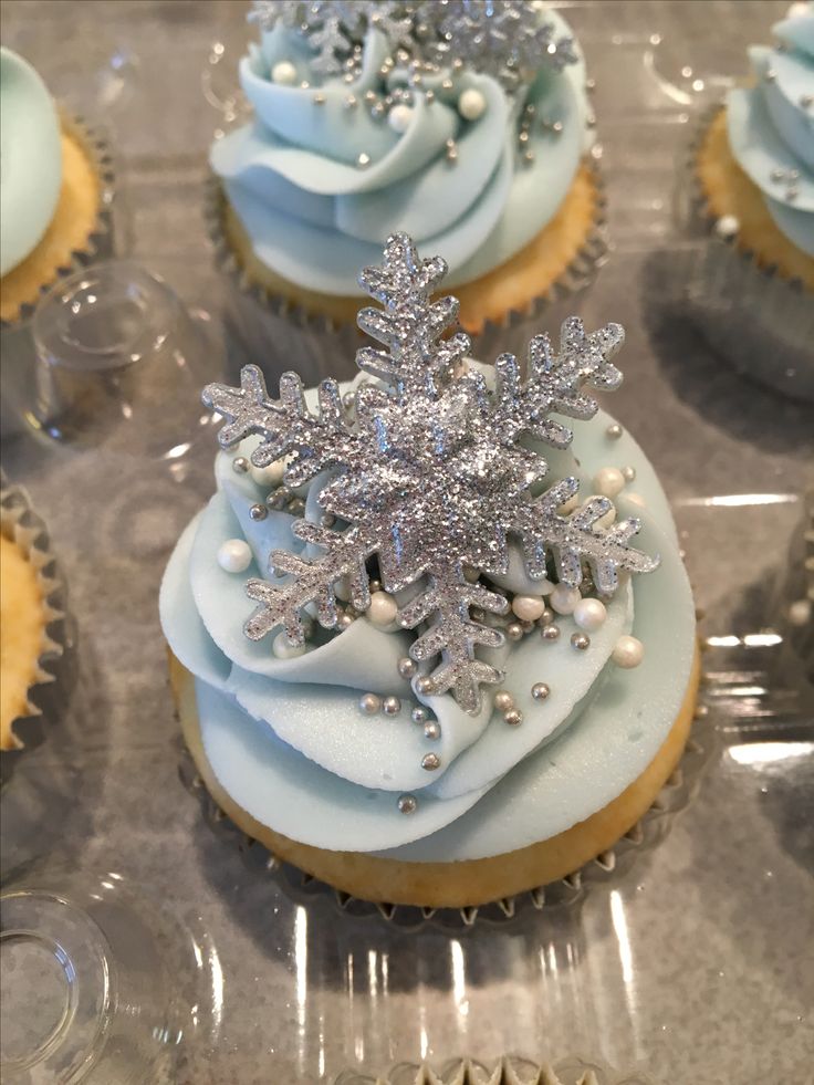 cupcakes decorated with frosting and snowflakes are displayed on a tray