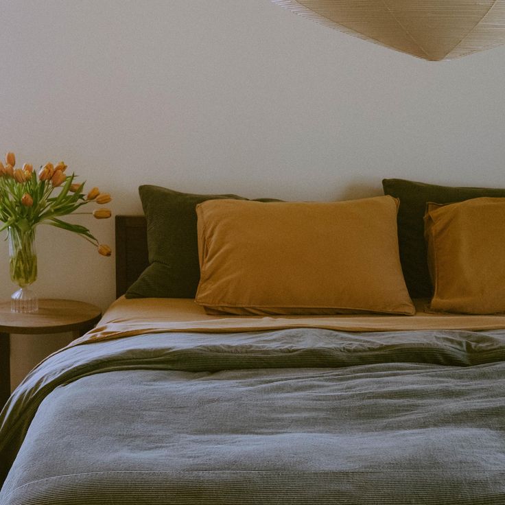 a bed with several pillows and two vases on the end table next to it