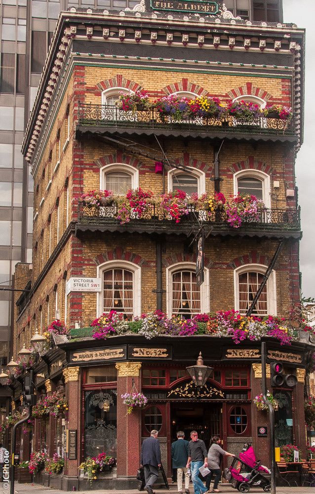 people are walking in front of a building with flowers on the balconies and windows