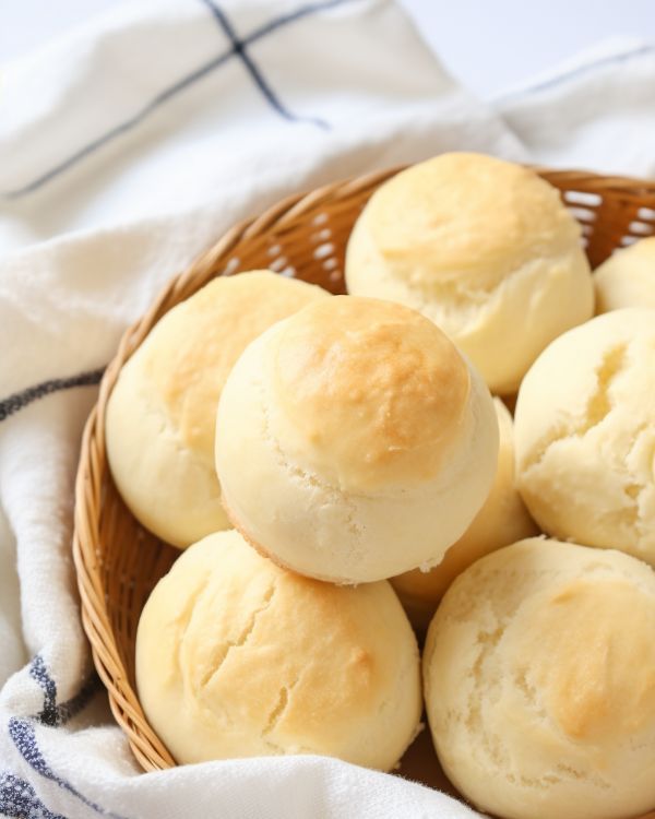 a basket filled with rolls sitting on top of a white table cloth next to a blue and white towel