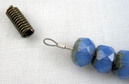 two blue beads sitting next to each other on a white tablecloth with a metal hook