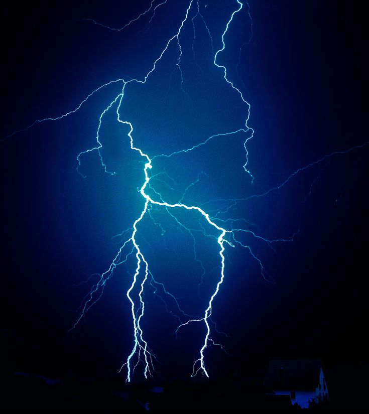 lightning strikes in the night sky above a house and tree line, with dark blue background