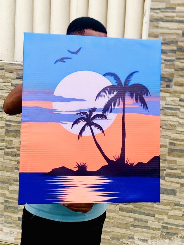 a man holding up a painting with palm trees and sunset in the background on it