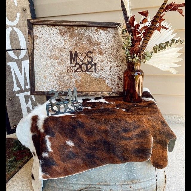 a cow hide covered table with flowers and other items on it's side, next to a home sign