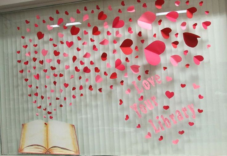 an open book sitting on top of a table next to a window covered in paper hearts