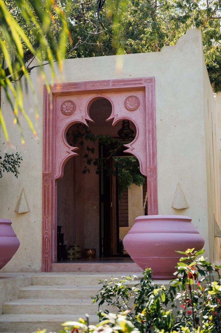 an entrance to a house with pink vases on the steps and trees in the background