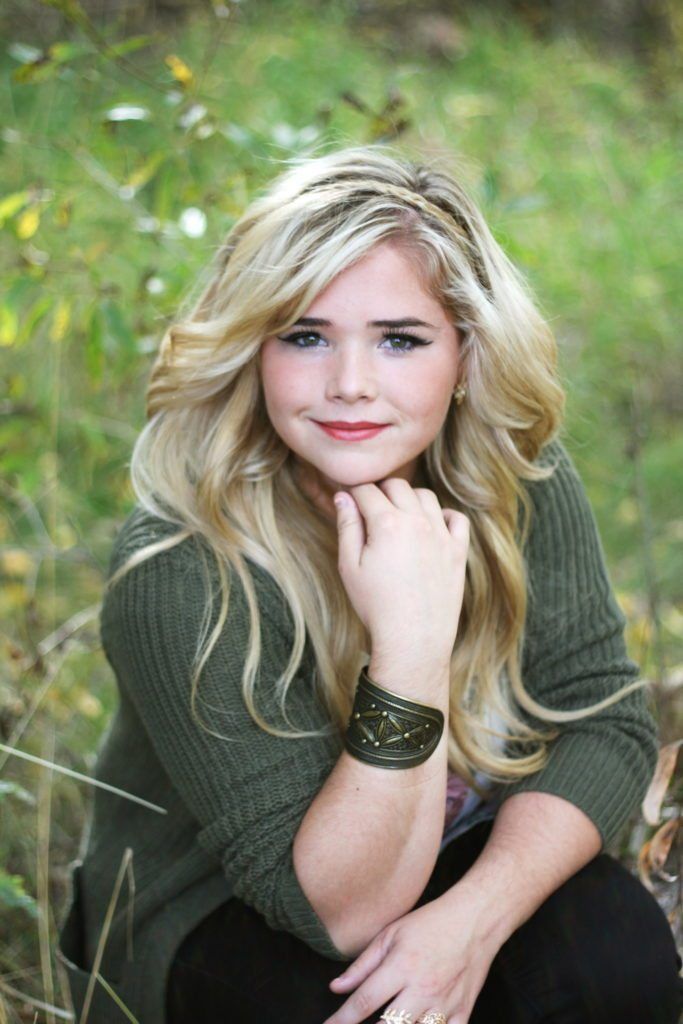 a woman sitting in the grass with her hand on her chin and looking at the camera