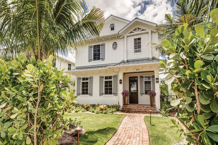 a white house surrounded by palm trees and bushes in the foreground is a brick path leading to it