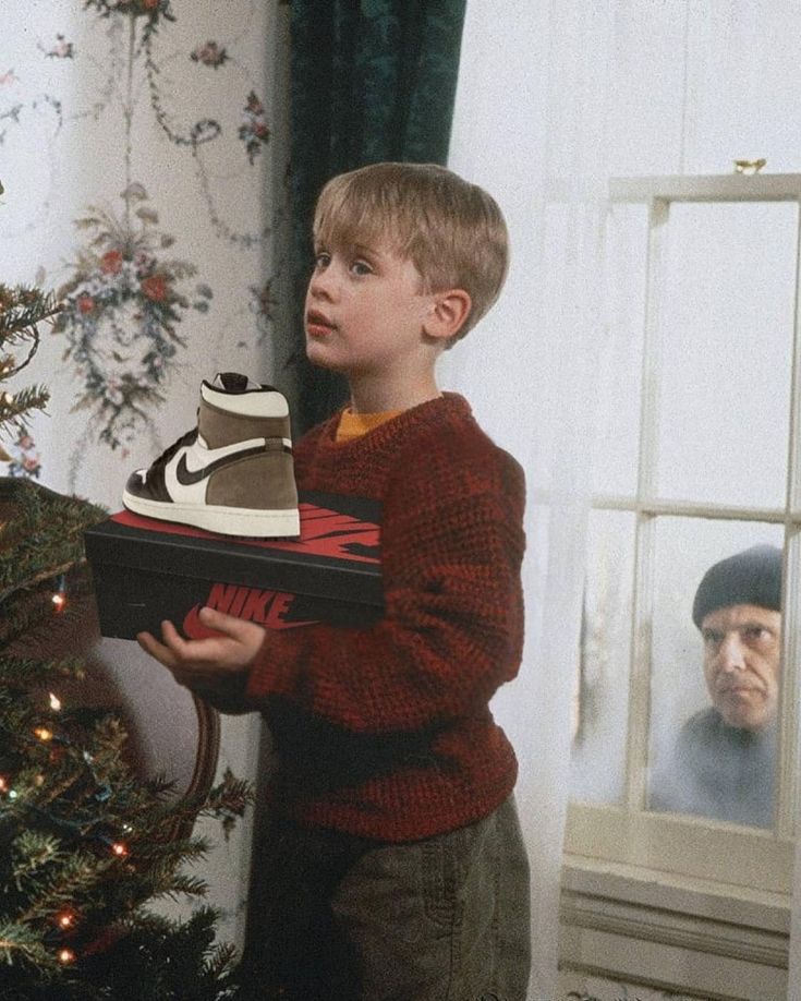 a young boy holding a shoe in front of a christmas tree